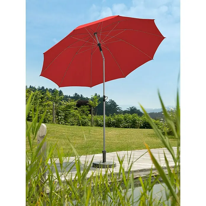 Schneider Classic Marktschirm rund Locarno - Rot, Durchmesser Bespannung: 220 cm - Ein roter Sonnenschirm steht auf einer Holzterrasse mit Blick auf einen Garten, ideal für sonnige Tage im Freien.