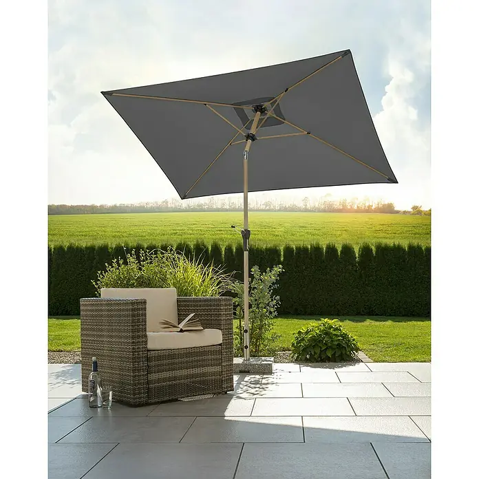 Schneider Classic Marktschirm Cordoba - Anthrazit, Bespannungsmaß (L x B): 230 x 150 cm - Quadratischer grauer Sonnenschirm spendet Schatten über einem Korbsessel mit Buch auf einer Terrasse.
