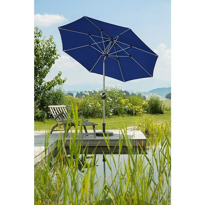 Schneider Classic Marktschirm rund Venedig - Blau, Durchmesser Bespannung: 270 cm - Eine Nahaufnahme eines blauen Sonnenschirms im Freien, der Schatten spendet, mit einem Holzstuhl und einem ruhigen Teich im Hintergrund.