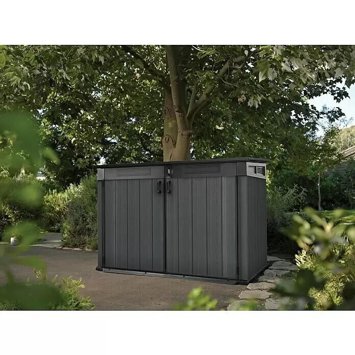Keter Truhe Cortina Mega - Außenmaß inkl. Dachüberstand (B x T): 191 x 109 cm, Kunststoff, Anthrazit/Schwarz - Dunkelgrauer Geräteschuppen aus Holzoptik-Kunststoff mit Doppeltüren im Garten unter einem Baum.