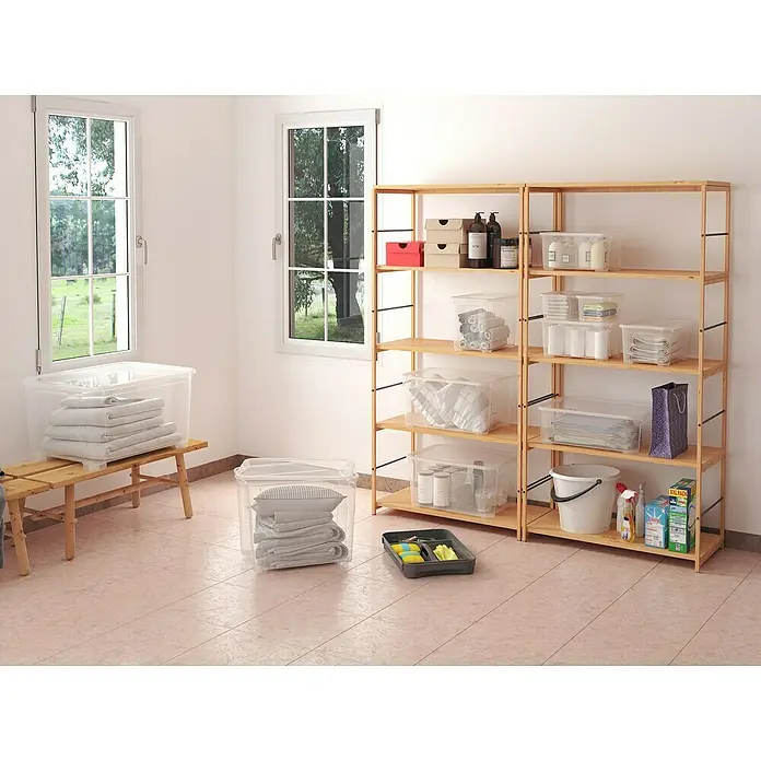 Regalux Aufbewahrungsbox Clear-Box - L x B x H: 54,8 x 38,4 x 28,3 cm, 47 l, Transparent - Ein Bild von hellen Holzregalen mit durchsichtigen Aufbewahrungsboxen und Reinigungsutensilien in einem Lagerraum, der durch Fenster natürlich beleuchtet wird.