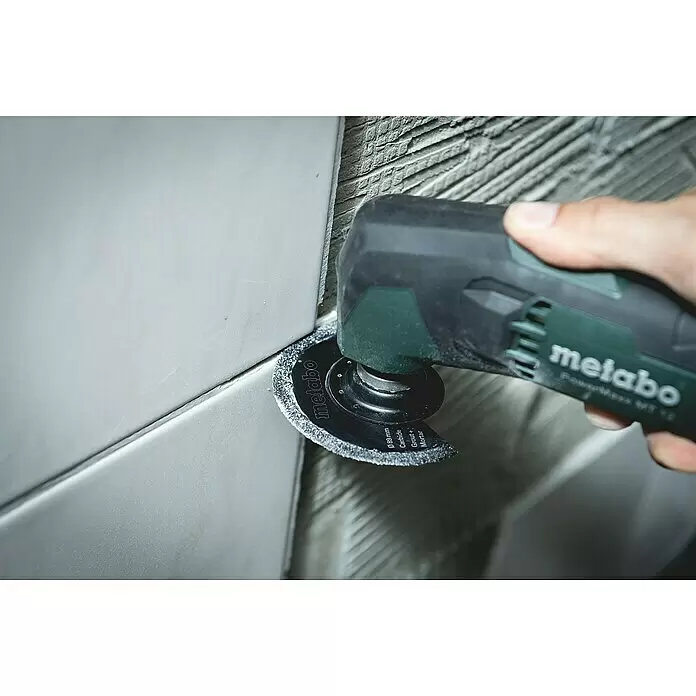 Metabo Akku-Multifunktionswerkzeug Powermaxx MT 12 - 12 V, 2 Akkus, 2 Ah - Metabo Akku-Multitool mit Hartmetall-Fugenfräser entfernt Fugen zwischen hellgrauen Fliesen.