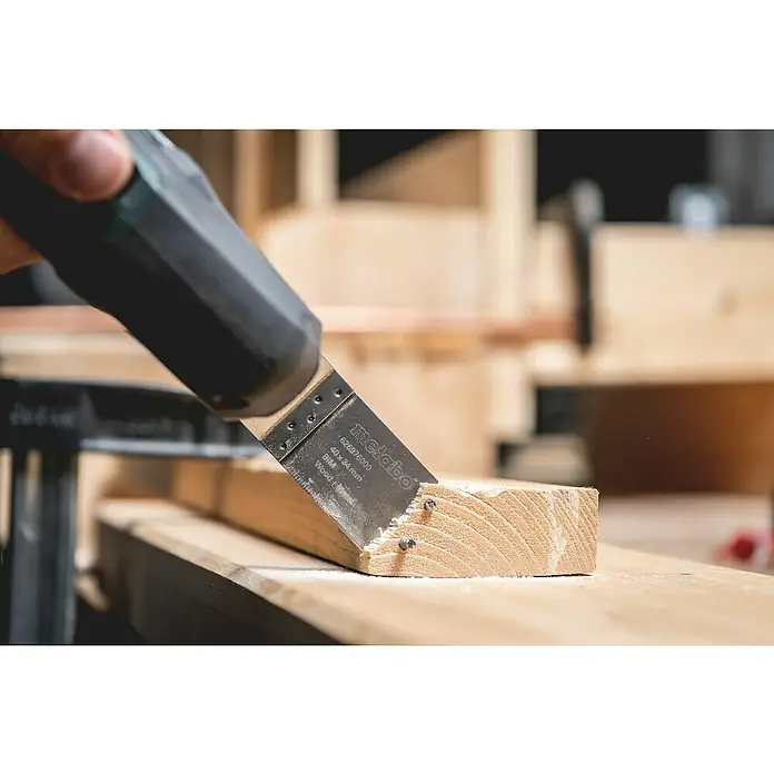 Metabo Akku-Multifunktionswerkzeug Powermaxx MT 12 - 12 V, 2 Akkus, 2 Ah - Das Bild zeigt ein Metabo-Multifunktionswerkzeug beim Sägen eines Holzstücks mit sichtbaren Nägeln. Die Marke Metabo ist deutlich erkennbar.