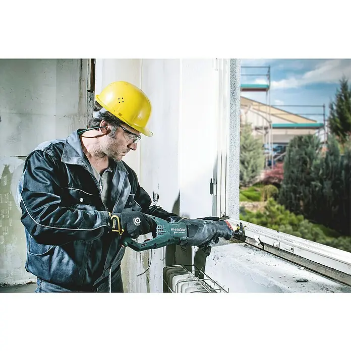 Metabo Säbelsäge SSEP 1400 MVT - 1.400 W, Hublänge: 32 mm - Ein Handwerker mit Schutzhelm benutzt eine Metabo Säbelsäge zum Schneiden, im Hintergrund ein Gebäude mit Gerüst.
