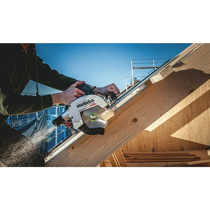 Metabo CAS 18V Akku-Handkreissäge KS 18 LTX 66 BL - 18 V, Ohne Akku, 4.800 U/min - Eine Metabo KS 18 LTX 66 BL Akku-Kreissäge schneidet ein Holzbrett, Sägespäne fliegen, im Hintergrund Gerüst und blauer Himmel.