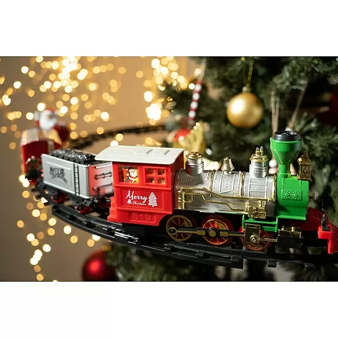 Elemento decorativo Tren LED - Colores surtidos, Plástico, 1 ud. - Tren de juguete navideño rojo, plateado y verde con detalles dorados sobre raíles, con figura de Papá Noel y texto "Merry Christmas", frente a luces festivas.