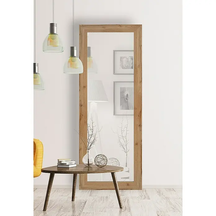 Espejo de pared DM Lisboa - 54 x 144 cm, Roble - Un espejo rectangular y estrecho con marco de madera apoyado contra una pared blanca, complementado por elementos decorativos en una mesa de madera.