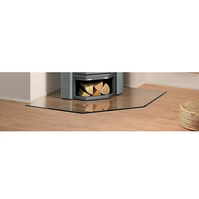 Justus Glasbodenplatte B5 - 110 x 110 cm, Fünfeckig - Nahaufnahme eines Kaminofens auf einer Glasbodenplatte, umgeben von einem Holzboden und einem Korbhocker für ein gemütliches Ambiente.