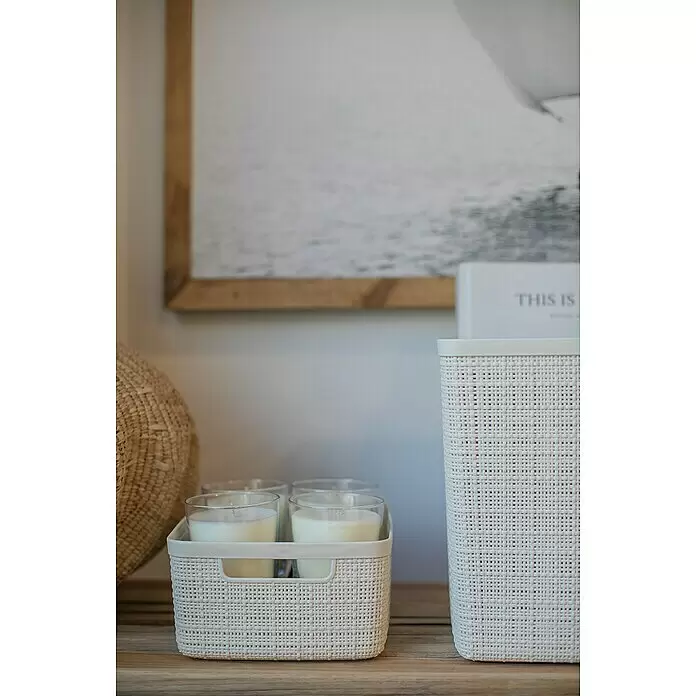 Curver Aufbewahrungsbox Jute - L x B x H: 27 x 20 x 11 cm, Kunststoff, Creme - Zwei cremefarbene Flechtkörbe auf einer Holzoberfläche; einer enthält Glas-Kerzen, der andere ist ein höherer, leerer Korb zur Heimorganisation.