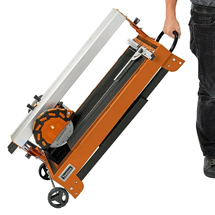 Toolson Elektro-Fliesenschneider PRO-RF 620 - 900 W, Max. Schnittlänge: 620 mm, Schnitttiefe bei 90 °: 30 mm - Das Bild zeigt eine Fliesenschneidmaschine mit Rollen und Griff zum einfachen Transport. Das Gerät ist orange und schwarz und verfügt über eine Schneidescheibe.