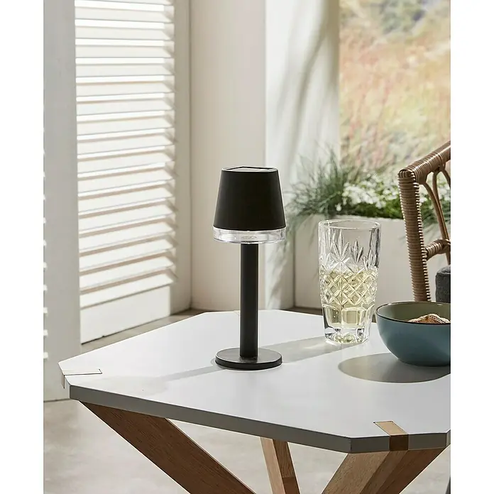 Luxform Cala D'Or Lámpara de sobremesa solar - Negro, IP44, Ø x Al: 8 x 22 cm - Lámpara de mesa negra junto a un vaso y un cuenco sobre una mesa blanca.