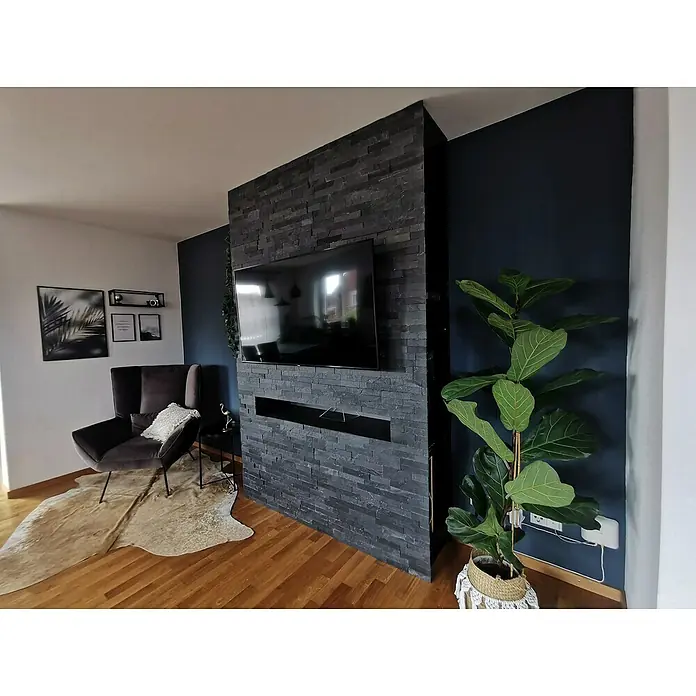 Verblendstein Nature - 15 x 60 cm, Schwarz, Steinoptik - Wohnzimmer mit dunkler Akzentwand, TV-Wand mit Steinverkleidung und elegantem Sessel auf einem stilvollen Teppich.
