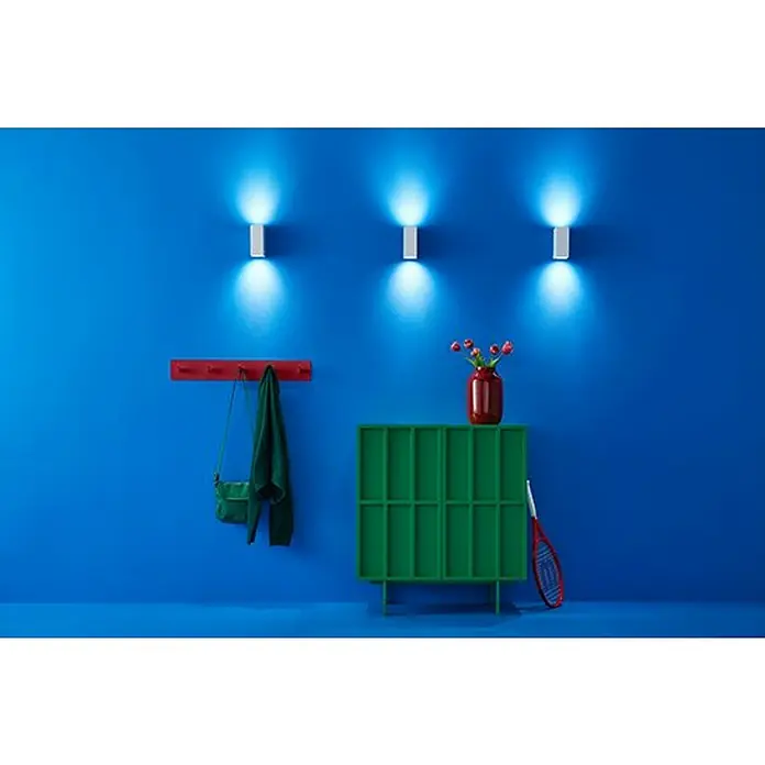 Philips Wiz LED-Außenwandleuchte Up & Down - 5 W, L x B x H: 9,2 x 6,8 x 15 cm, Weiß, RGBW - Wandleuchten erhellen eine blaue Wand über einer grünen Kommode, einem roten Kleiderhaken und dekorativen Gegenständen.