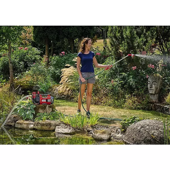 Einhell Power X-Change 18V Akku-Gartenpumpe AQUINNA 18/30 F LED - 18 V, Ohne Akku, Max. Fördermenge: 3.000 l/h - Frau bewässert Gartenpflanzen aus Teich mit rot-schwarzer Pumpe.