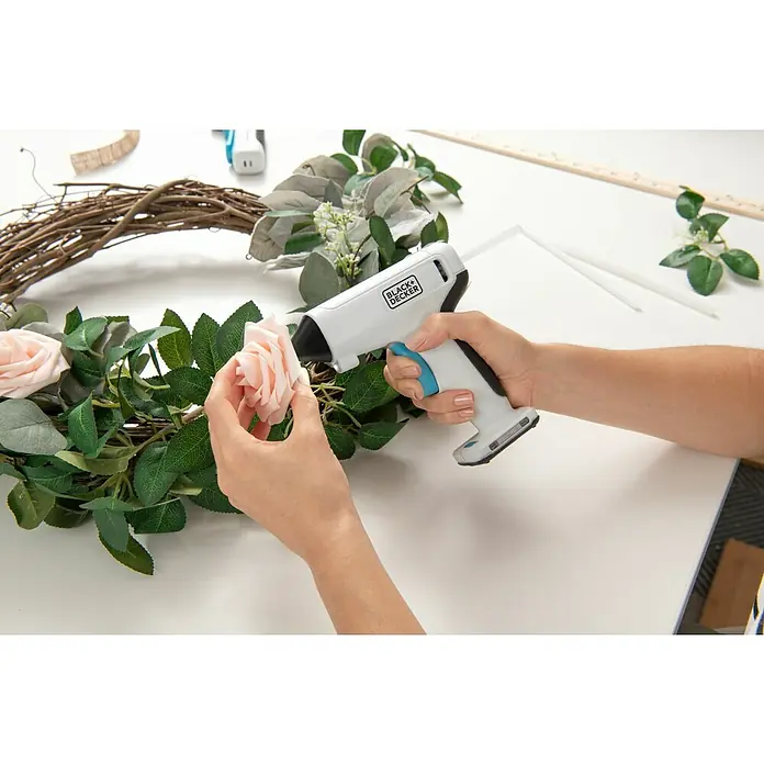 Black+Decker Pistola termoencoladora con batería BCGL115 3,6V-Li - 3,6 V - Una persona está fijando una rosa rosa a una corona floral con una pistola de pegamento BLACK+DECKER.