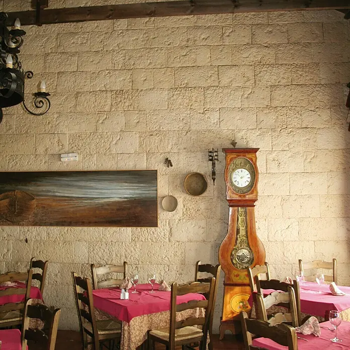 Revestimiento de piedra Coral Piedra - Coral - Elegante restaurante con un antiguo reloj de pie. El ambiente acogedor se complementa con manteles rosas y sillas de madera tradicionales.