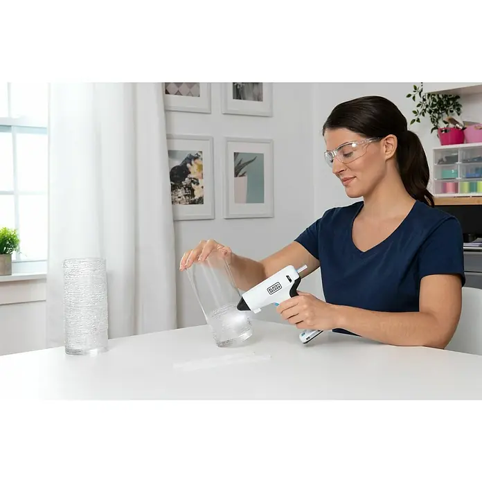 Black+Decker Pistola termoencoladora con batería BCGL115 3,6V-Li - 3,6 V - Una mujer usa una pistola de pegamento Black+Decker en un cilindro de vidrio para proyectos creativos de bricolaje.