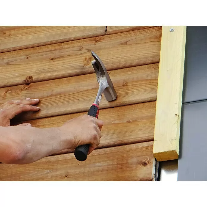 Peddinghaus Zimmermannshammer - 600 g, Kunststoff, Magnetischer Nagelhalter - Eine Person hämmert Holzverkleidung mit einem Klauenhammer mit schwarz-rotem Griff.