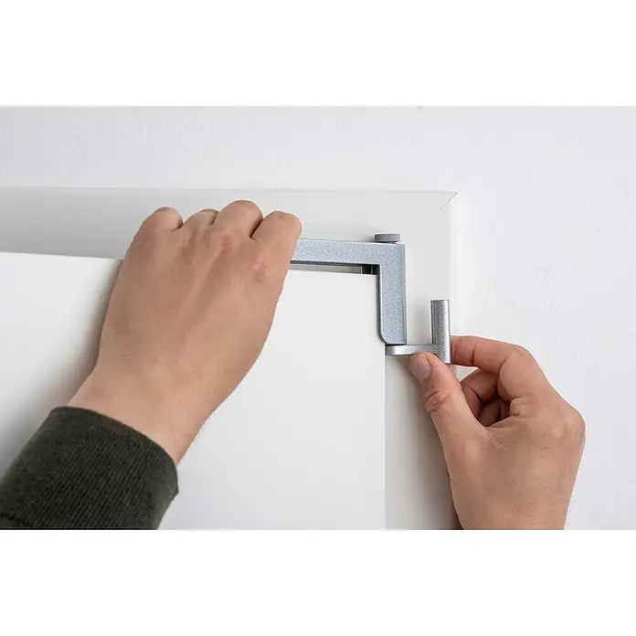 Abus Türschließer 2603 - Geeignet für: Innentüren, L x B: 125 x 70 mm, Links/Rechts, Silber - Anbringen eines silberfarbenen Türhängers an einer weißen Tür, wobei die Hand den Hänger fixiert.