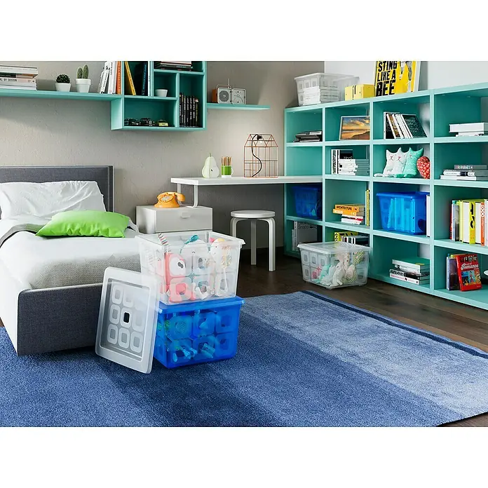 KIS Aufbewahrungsbox K LATCH - L x B x H: 59 x 39 x 28 cm, Transparent - Diese Aufnahme zeigt dekorative blaue und transparente Aufbewahrungsboxen, die auf einem blauen Teppich neben einem Bett platziert sind.