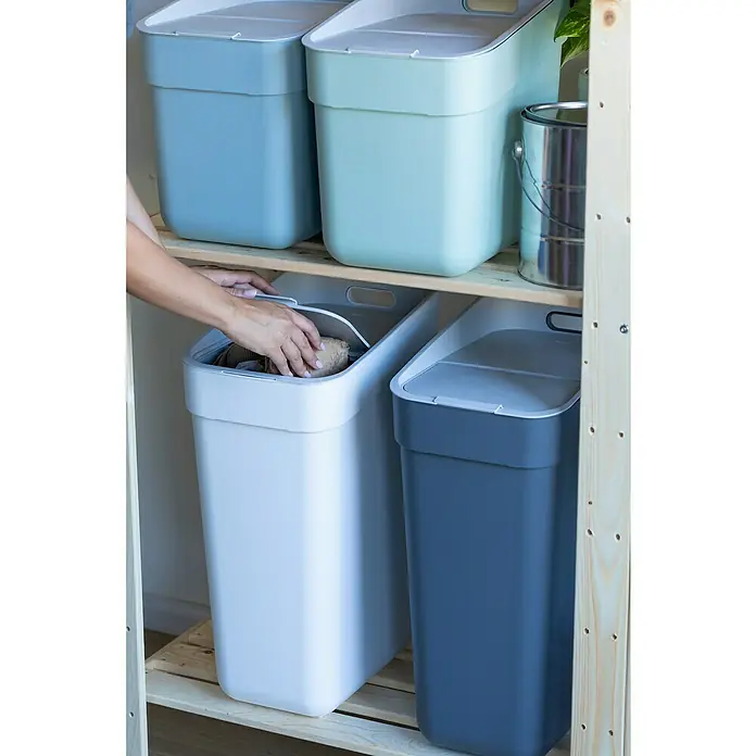Curver Standard Mülleimer Ready to Collect - 30 l, Kunststoff, Weiß - Aufnahme eines Mehrzweckbehälters, der in einem Regal steht, mit einer Person, die ihn öffnet, um etwas hineinzulegen, mit anderen bunten Behältern.