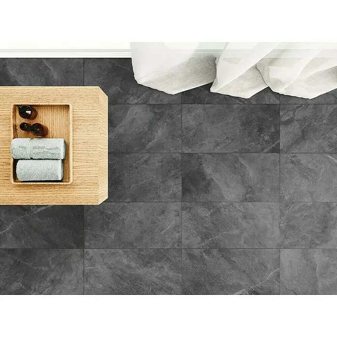 Domicil Feinsteinzeugfliese Stone Art - 30 x 60 cm, Smoke Anthrazit, Matt - Draufsicht eines Badezimmers mit grauen Fliesen, einem Holztisch mit Handtüchern und Ölflaschen sowie weissen Vorhängen.