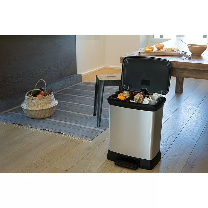 Keter Treteimer Deco Bin Metallics Duo - 30 l, Metall, Schwarz/Silber - Edelstahl-Mülleimer mit offenem schwarzem Deckel, zeigt Innenfächer zur Mülltrennung neben einem Tisch mit vorbereiteten Früchten.