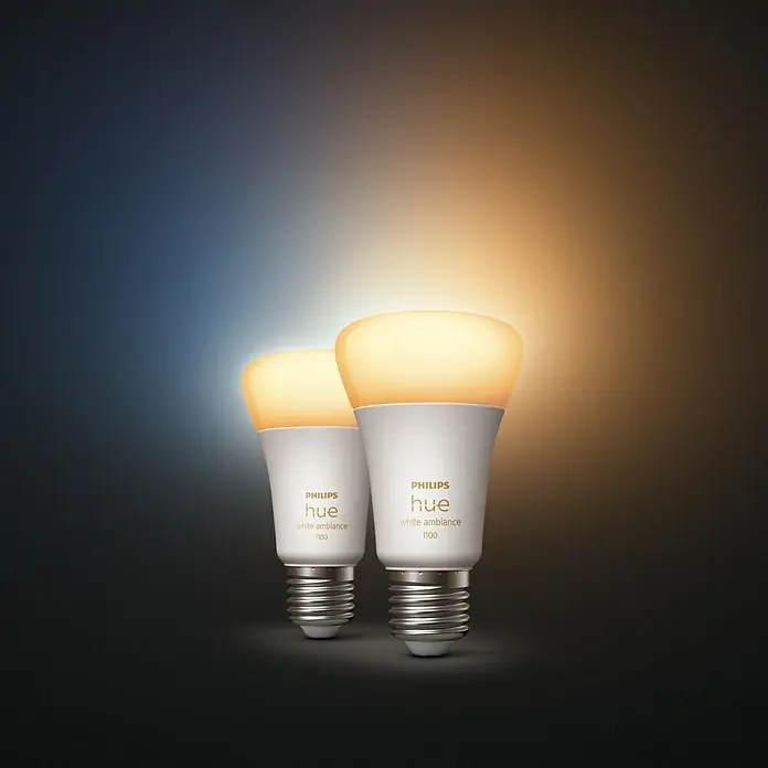 Philips Hue Smart-LED-Lampen Set White Ambiance - E27, Dimmbar, Warmweiß, 1.100 lm, 8 W, 2 Stk. - Zwei Philips Hue White Ambiance 1100 Glühbirnen, die warmes Licht ausstrahlen, stehen vor einem farbigen Hintergrund.