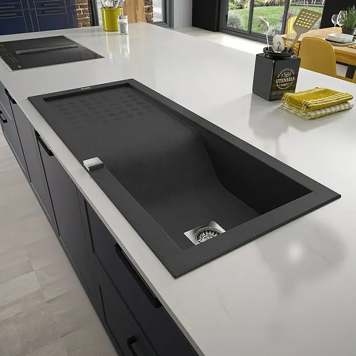 Carea Einbauspüle Vague - 118 x 50 cm, Schwarz, Material Spüle: CAREAgranit® - Nahaufnahme eines modernen schwarzen Spülbeckens mit Abtropffläche auf einer weißen Kücheninsel.