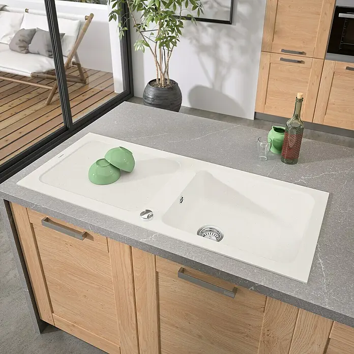 Carea Einbauspüle Botia - 118 x 50 cm, Weiß, Material Spüle: CAREAlith® - Nahaufnahme einer weißen Spüle mit zwei Becken und grauer Arbeitsplatte, umgeben von Holzküchenschränken.