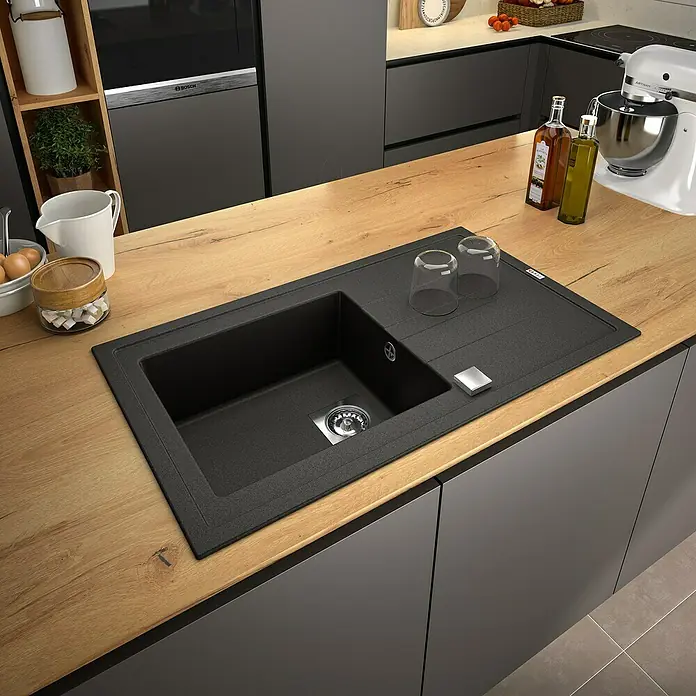 Carea Fregadero encastrable Tango - 86 x 50 cm, Negro, Material del fregadero: CAREAgranit - Fregadero de cocina negro con escurridor, encastrado en una encimera de madera, con armarios grises debajo. Hay vasos sobre el fregadero.