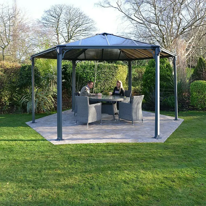 Palram – Canopia Pérgola estándar Mónaco - An x Pr: 390 x 450 cm, Color del armazón: Antracita, Aluminio - Escena de jardín con una elegante glorieta con mesa y sillas, ideal para relajarse al aire libre.