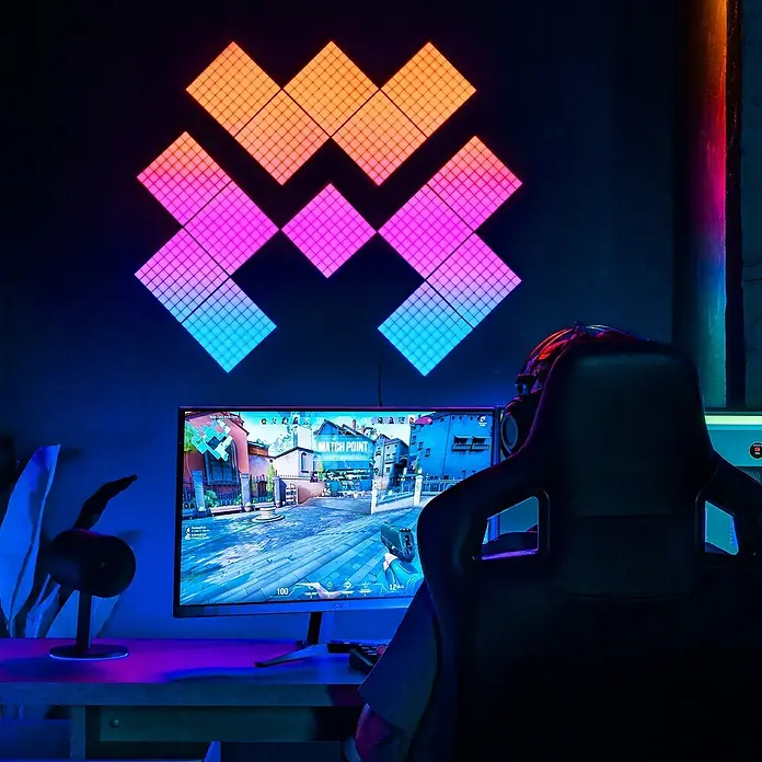 Twinkly LED-Panel-Set Squares RGB StartersetRGB - Farbige, modulare Nanoleaf-Lichtpaneele an der Wand über einem Gamer-PC.