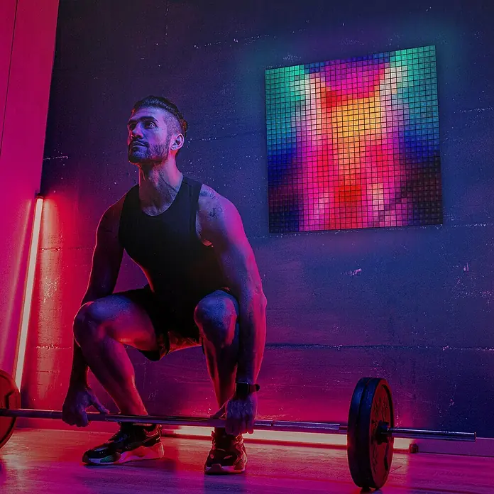 Twinkly LED-Panel-Set Squares RGB StartersetRGB - Athlet beim Gewichtheben vor einer bunten Nanoleaf-Wand, die dynamisches Licht ins Fitnessstudio bringt und die Trainingsatmosphäre verbessert.