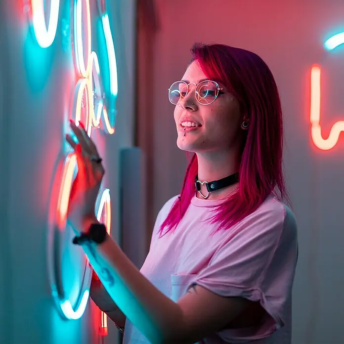 Twinkly LED-Lichtschlauch Flex - Länge: 2 m, Lichtfarbe: RGB, 15 W - Frau mit runder Brille und pinkfarbenem Haar, die Neonkunst berührt. Ein trendiger und moderner Look mit einzigartigem Stil.