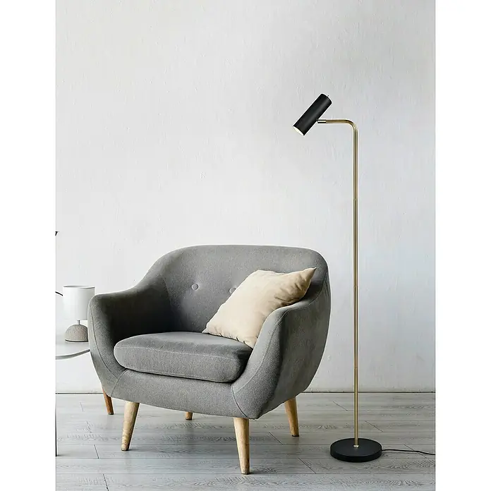 Trio Lighting Marley Lámpara de pie - 5 W, Altura: 151 cm, Dorado/Negro, GU10 - Una lámpara de pie moderna con soporte dorado y pantalla negra está al lado de un sillón gris con almohada.