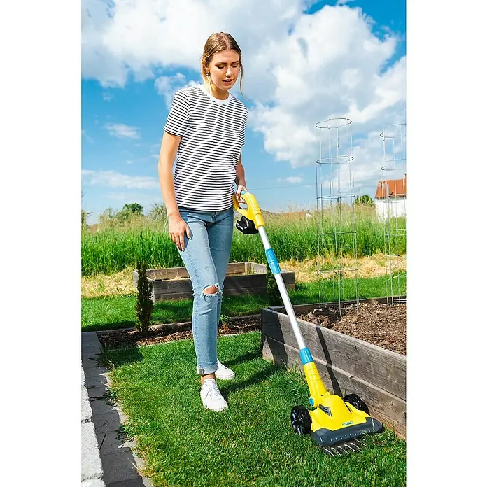 Gloria Power for All 18V Akku-Rasenmäher Grasschere FineCut 18V - 18 V, Ohne Akku, Schnittbreite: 25 cm - Eine Frau benutzt einen gelben und blauen Vertikutierer im Garten, um den Rasen zu pflegen. Der Vertikutierer lockert den Boden auf.