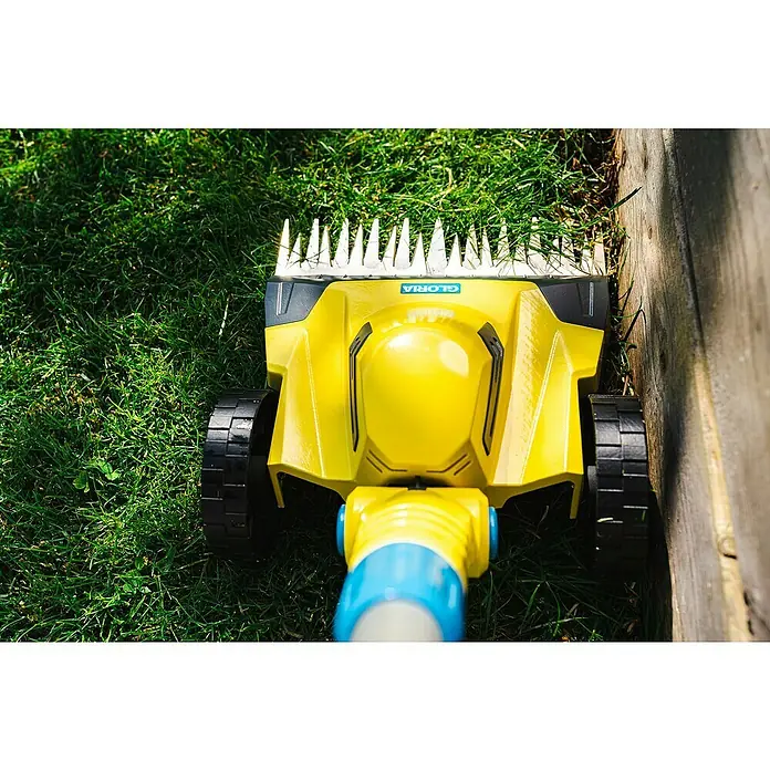 Gloria Power for All 18V Akku-Rasenmäher Grasschere FineCut 18V - 18 V, Ohne Akku, Schnittbreite: 25 cm - Der Gloria Grasschneider im Einsatz, um Rasenkanten sauber zu trimmen. Das gelbe Gerät steht auf grünem Gras neben einem Holzzaun.