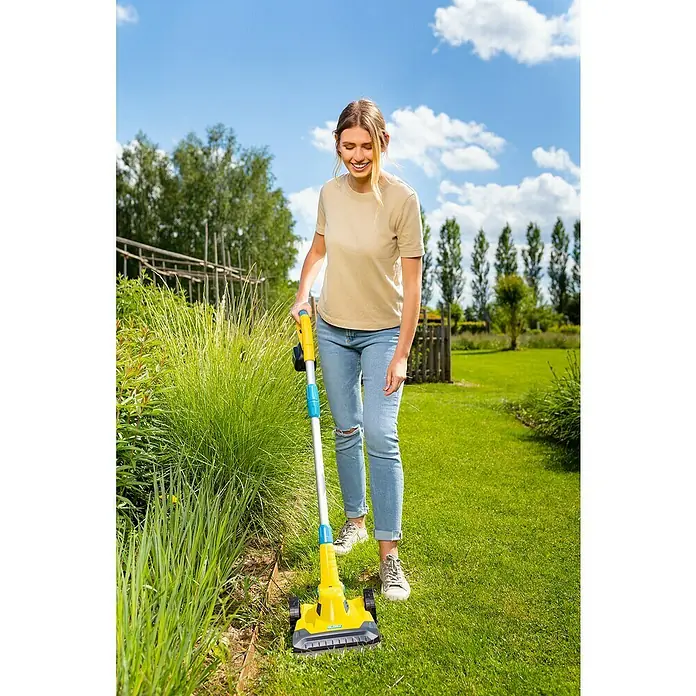 Gloria Power for All 18V Akku-Rasenmäher Grasschere FineCut 18V - 18 V, 1 Akku, Schnittbreite: 25 cm - Eine Frau benutzt einen gelben Unkrautentferner mit Rädern, um Unkraut in ihrem Garten zu entfernen.