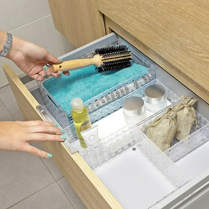 Organizador Remontable - L x An x Al: 16 x 11 x 6,5 cm, Número de compartimentos: 1 ud., Translúcido - Cajón abierto de armario de baño con contenedores de almacenamiento transparentes, llenos de artículos de tocador y una mano sosteniendo un cepillo.