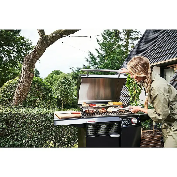 Char-Broil Elektrogrill Smart E - Grillfläche (B x T): 57 x 39 cm, 2,4 kW - Eine Frau grillt auf einem hochwertigen Grill im Freien, Gemüse und Fleisch liegen auf dem Rost.