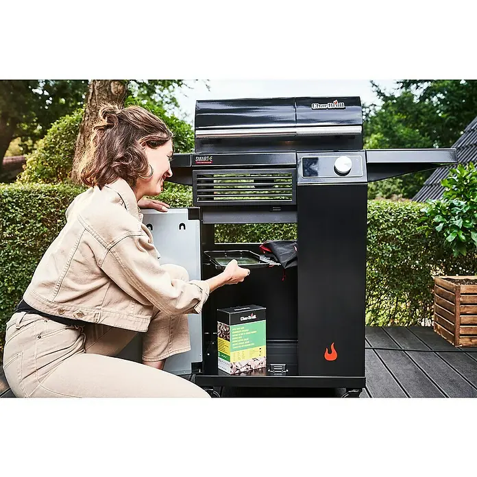 Char-Broil Elektrogrill Smart E - Grillfläche (B x T): 57 x 39 cm, 2,4 kW - Frau hockt neben einem Char-Broil SMART-E Elektrogrill und legt ein Tablett in das Gerät.