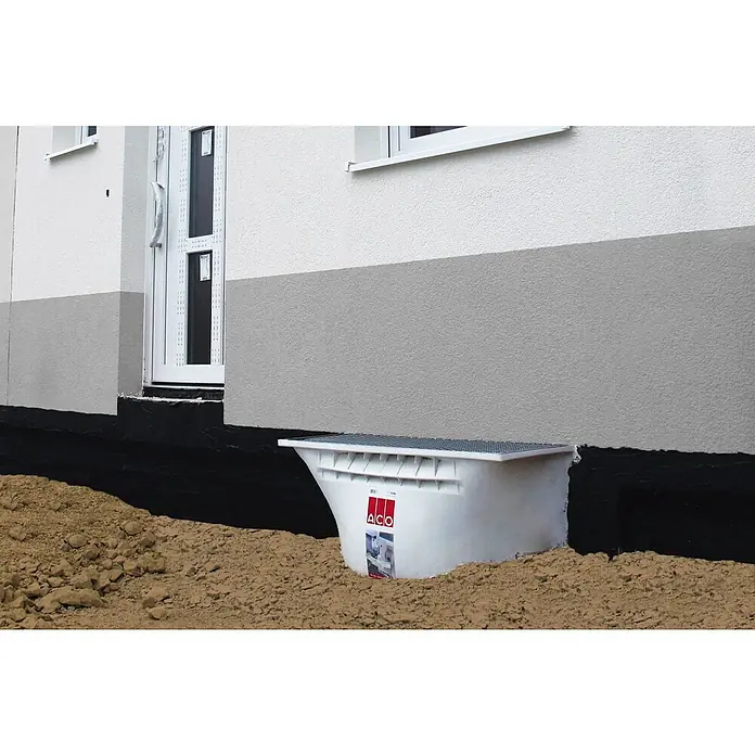 ACO Therm Lichtschacht-Set - 60 x 100 x 100 cm, Polypropylen - Nahaufnahme eines ACO-Lichtschachts mit Gitterrost vor einer Hauswand, eingebettet in Erdreich, das Tageslicht und Belüftung für Kellerräume bietet.