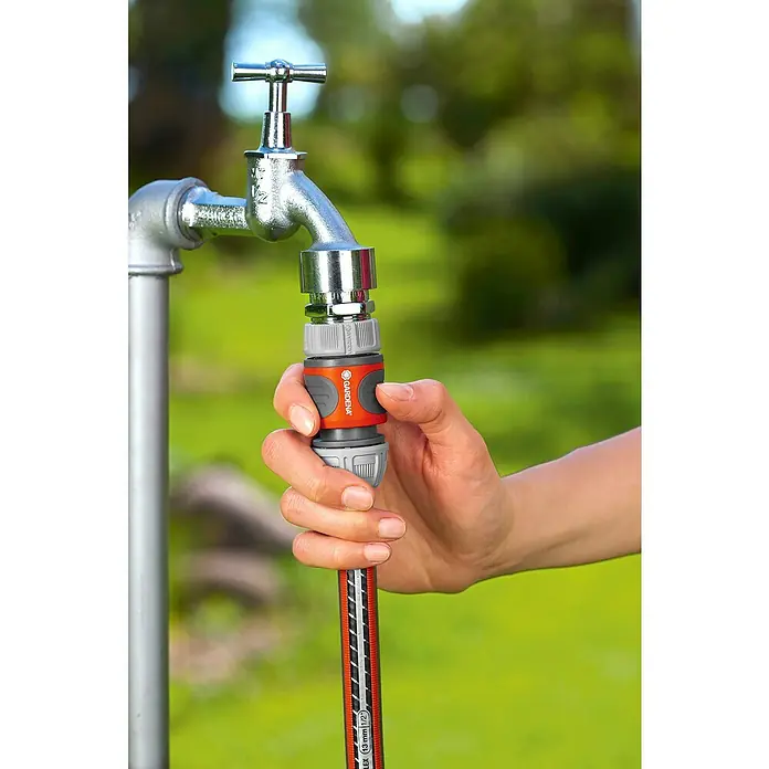 Gardena Schlauchkupplung - ½″ / ⁵⁄₈″ - Nahaufnahme eines Wasserhahns mit Gardena-Schlauchkupplung, die von einer Hand bedient wird, um einen Gartenschlauch anzuschließen.