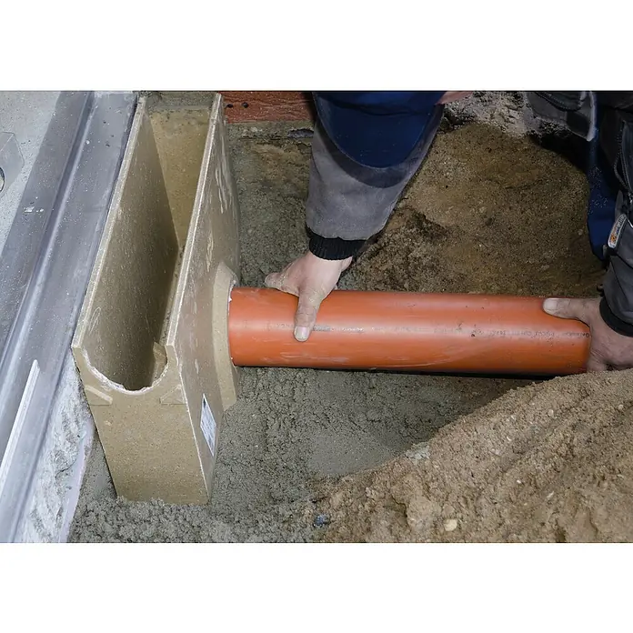 ACO Self Einlaufkasten Standardline - 50 x 11,8 x 30 cm - Ein Handwerker installiert ein orangefarbenes Abwasserrohr in einem Entwässerungssystem mit einem Schacht aus Betonfertigteilen.