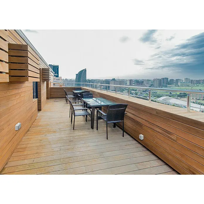 Siemens Delta IP54 Feuchtraumtaster SIE028653 - Grau, Aufputzmontage, IP54 - Einladende Terrasse mit dunklen Rattan-Gartenmöbeln und einem atemberaubenden Ausblick auf die Stadt unter bewölktem Himmel.
