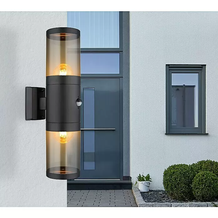 Globo Xeloo Sensor-Außenleuchte - 60 W, L x B x H: 10,2 x 10,2 x 42 cm, Schwarz, IP44, Bewegungsmelder - Schwarze zylindrische Außenwandleuchte mit amberfarbenem Glas, zwei Leuchtmitteln und Bewegungssensor, montiert an einer weißen Hausfassade.