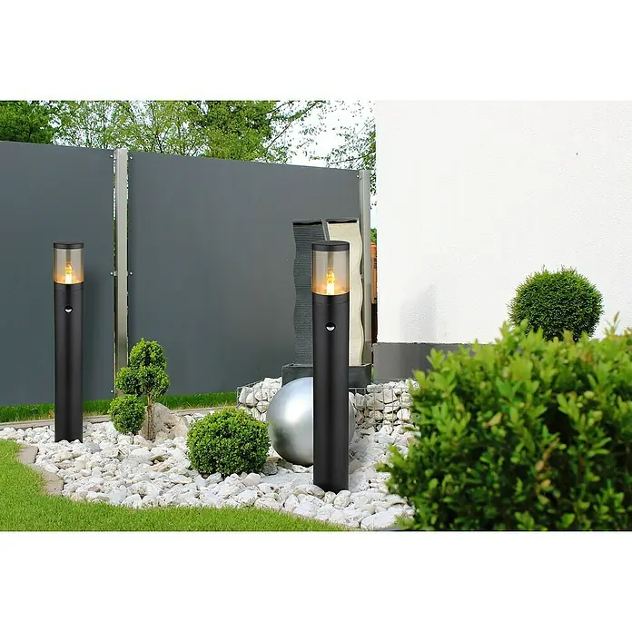Globo Xeloo Außensockelleuchte - 60 W, Schwarz, 14 x 80 cm - Ein elegantes Bild von zwei schwarzen Gartenlampen, die den Außenbereich mit ihrem warmen Licht aufwerten. Die Lampen stehen auf weißen Steinen.