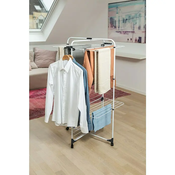 Vileda Turm-Wäscheständer Level 3 - Länge Wäscheleine: 33 m, L x B x H: 69 x 74 x 130 cm, Weiß/Anthrazitgrau - Ein Wäscheständer mit verschiedenen Kleidungsstücken, darunter Hemden, Hosen und Handtücher. Der Ständer steht auf einem Holzboden.