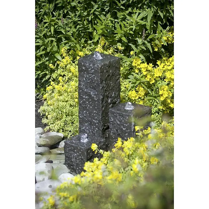 Ubbink AcquaArte Einbaubrunnen Taranto - Naturmaterialien, Dunkelgrau - Drei moderne dunkle Gartenbrunnen mit gelben Blumen und grünen Pflanzen im Hintergrund. Die Brunnen sprudeln Wasser an der Spitze.